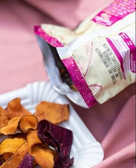 Sweet potato chips on a white plate next to white and pink chip bag