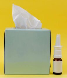 Bottle of nasal spray beside a green facial tissue box on a yellow background