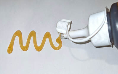 Squiggle of orange glue from a bottle with a white cap, both against a white background.
